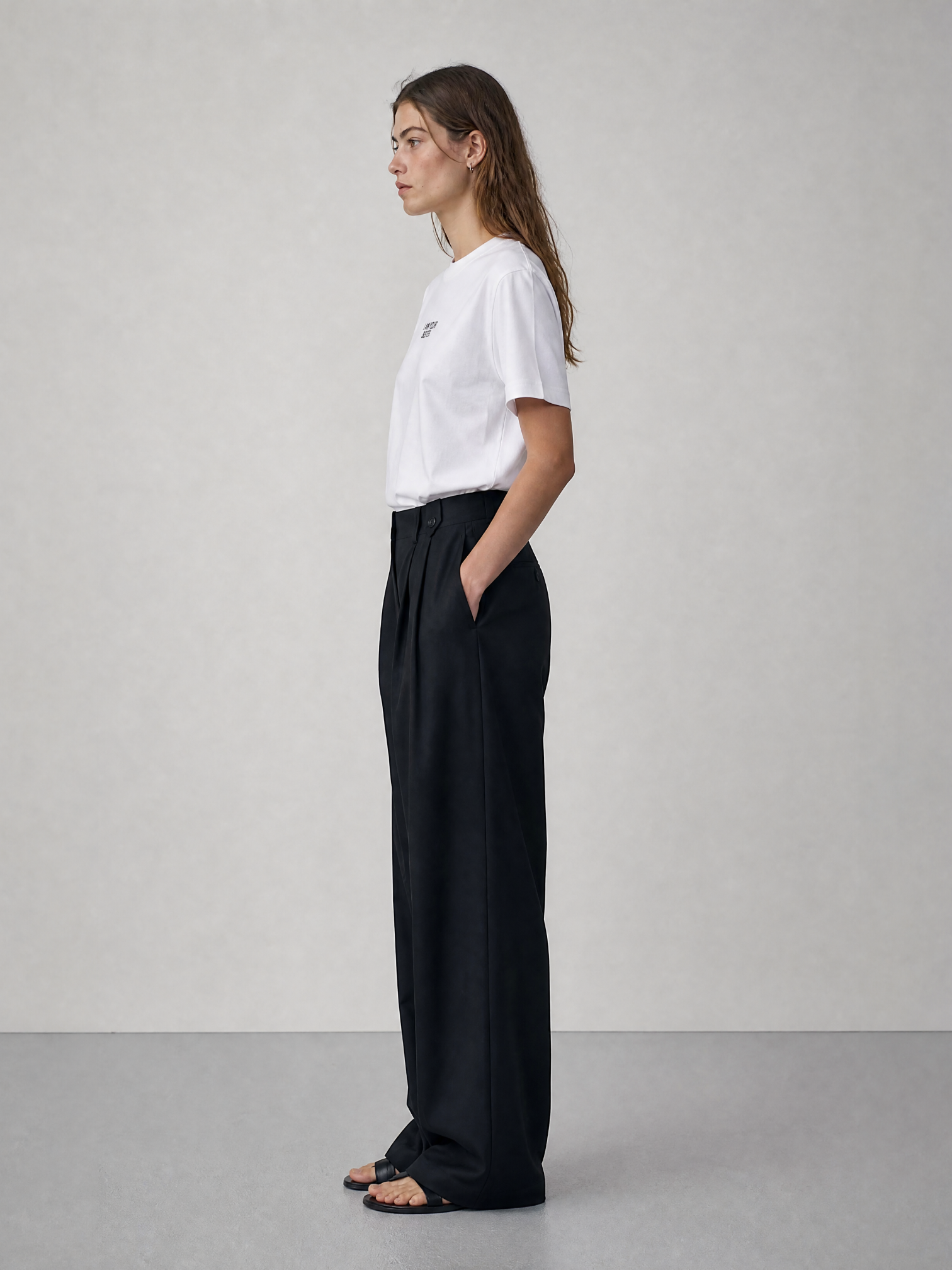 Woman wearing a white t-shirt and black pants against a plain background