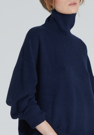 Closeup of a navy turtleneck cashmere sweater with ribbed trims, displayed on a woman with a neutral expression.