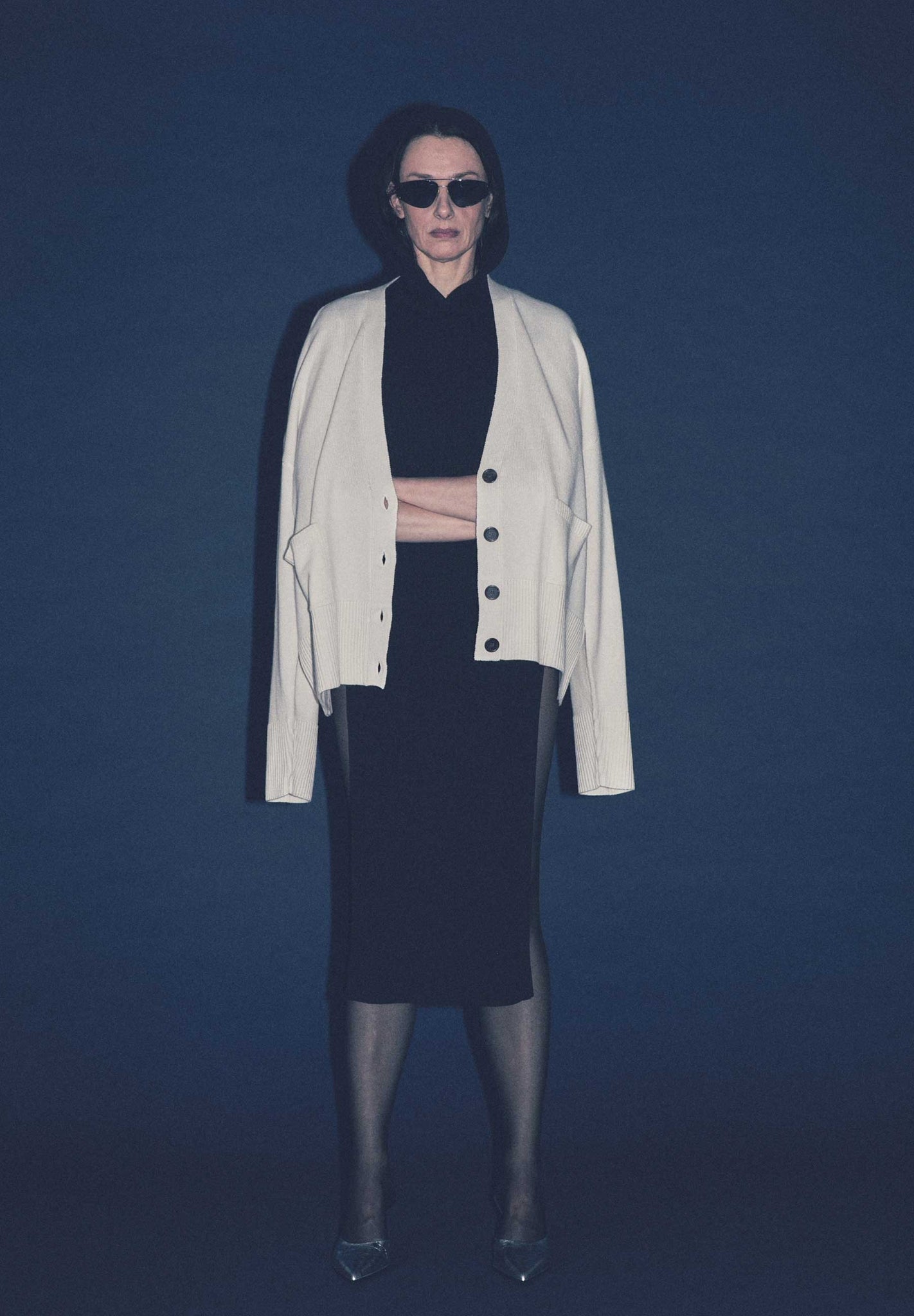 Woman wearing a luxury cream colored cashmere  cardigan over a black outfit against a dark blue background