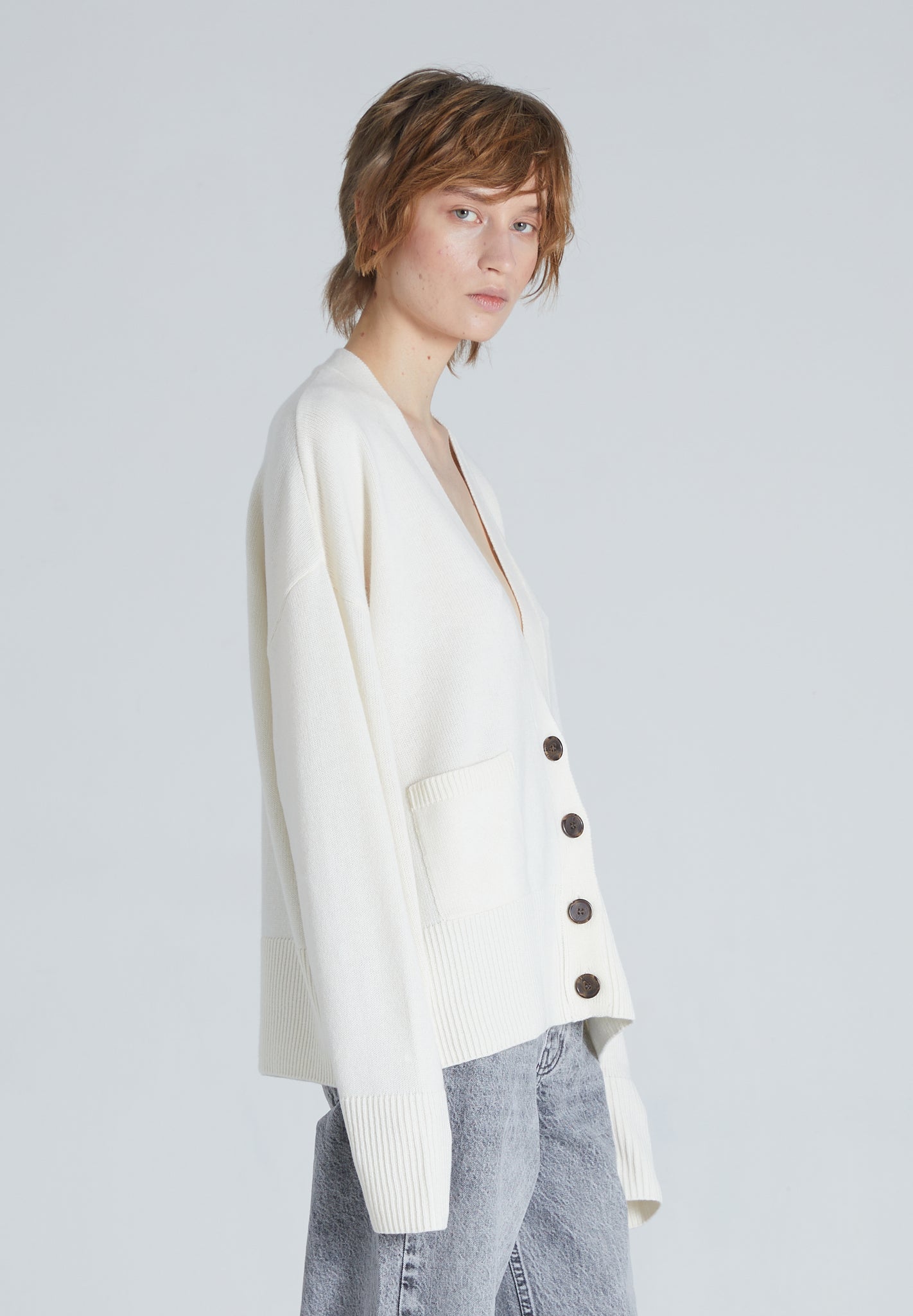 Side of a woman wearing luxury Cream colored cashmere cardigan with relaxed fit and long sleeves.
