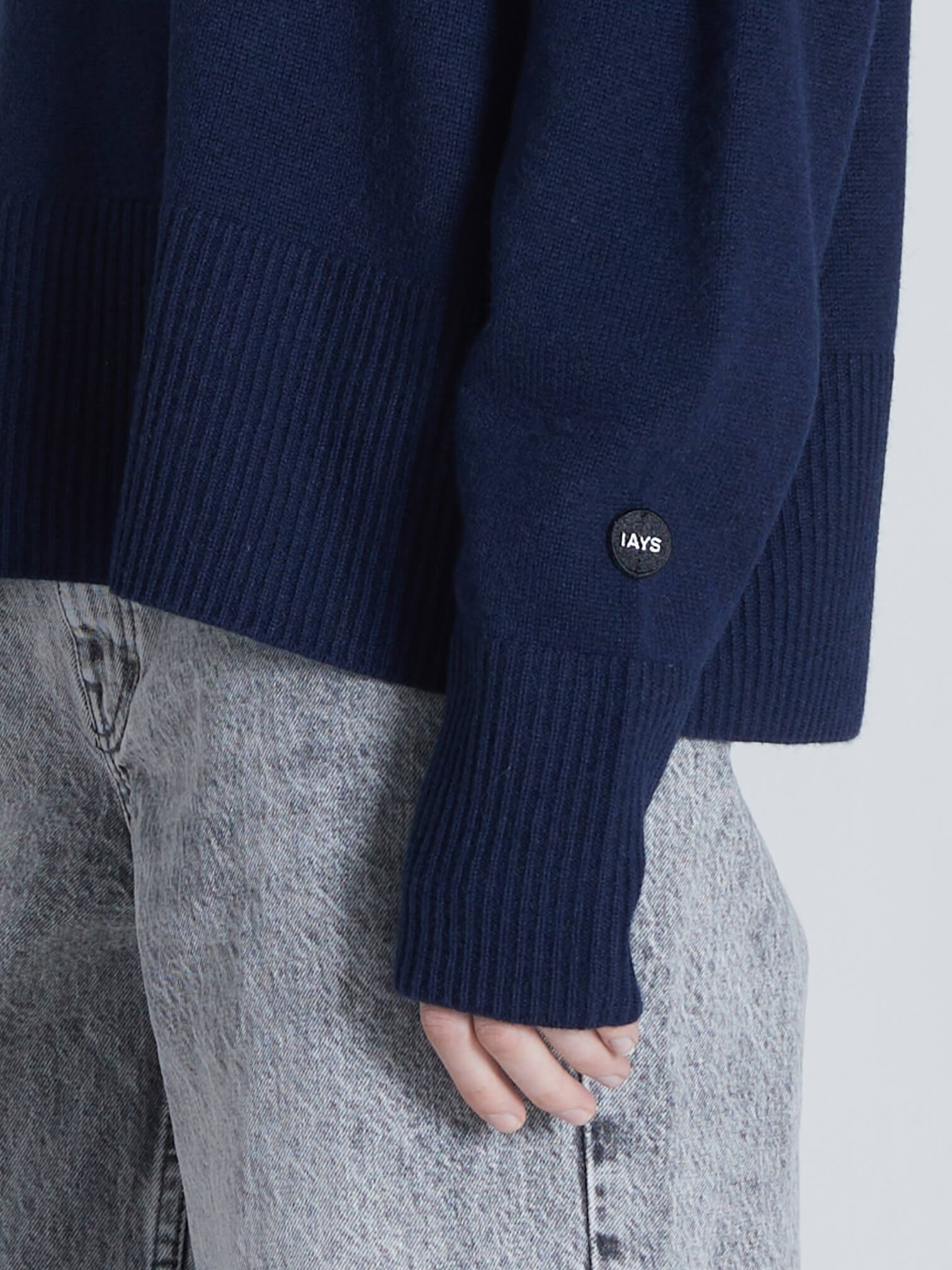 Navy sweater with a brand logo worn by a person, on a light gray background