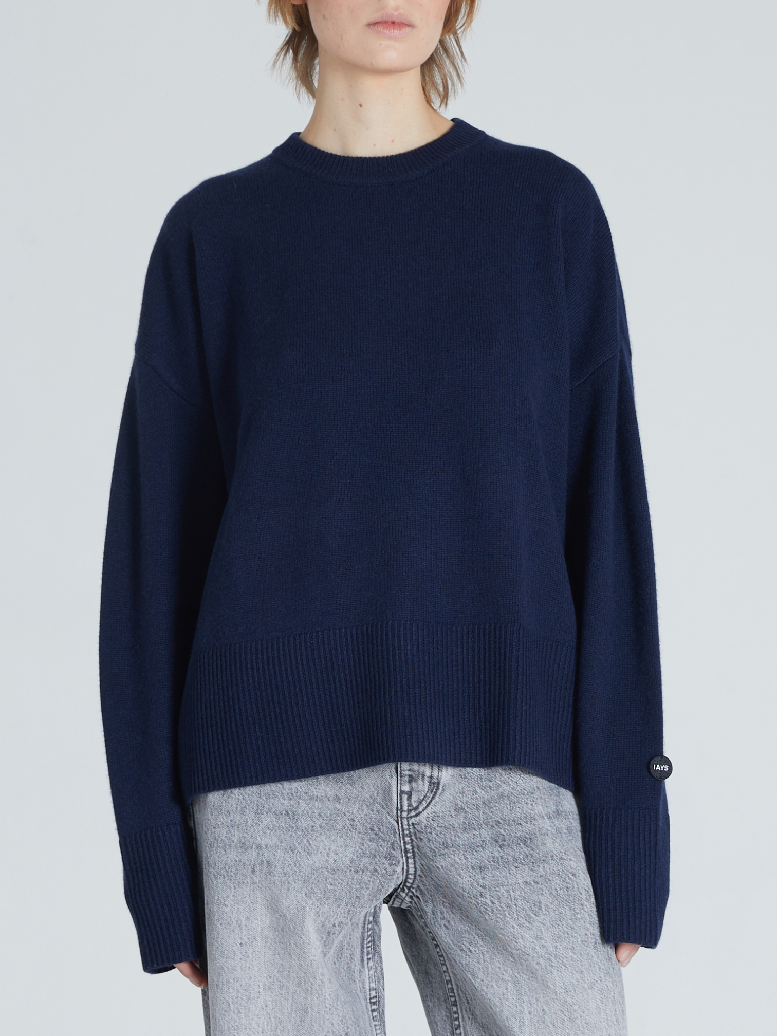 A model wearing an oversized navy blue knit sweater with ribbed cuffs and hem, paired with light-wash jeans, against a light gray studio background.