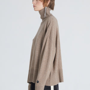 Woman wearing a high-end brown cashmere turtleneck. She also wears black pants and a silver earring 