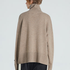 Back of woman wearing brown cashmere turtleneck. She is also wearing black trousers. 