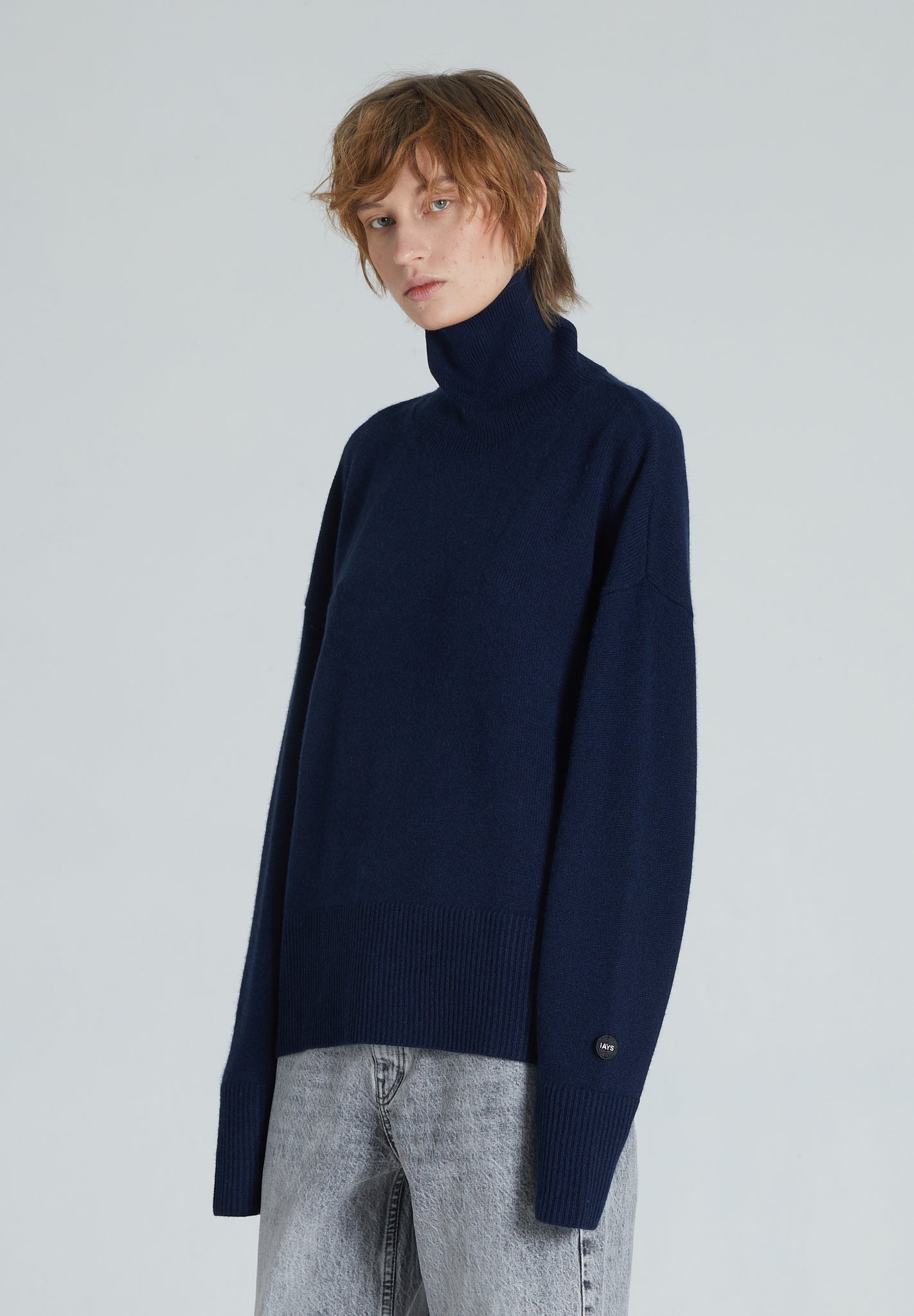 A navy turtleneck cashmere sweater with ribbed trims, displayed on a woman with a neutral expression.