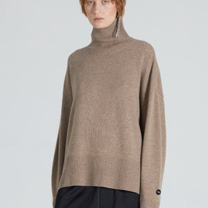 A woman wearing a brown turtleneck cashmere sweater and black trousers.