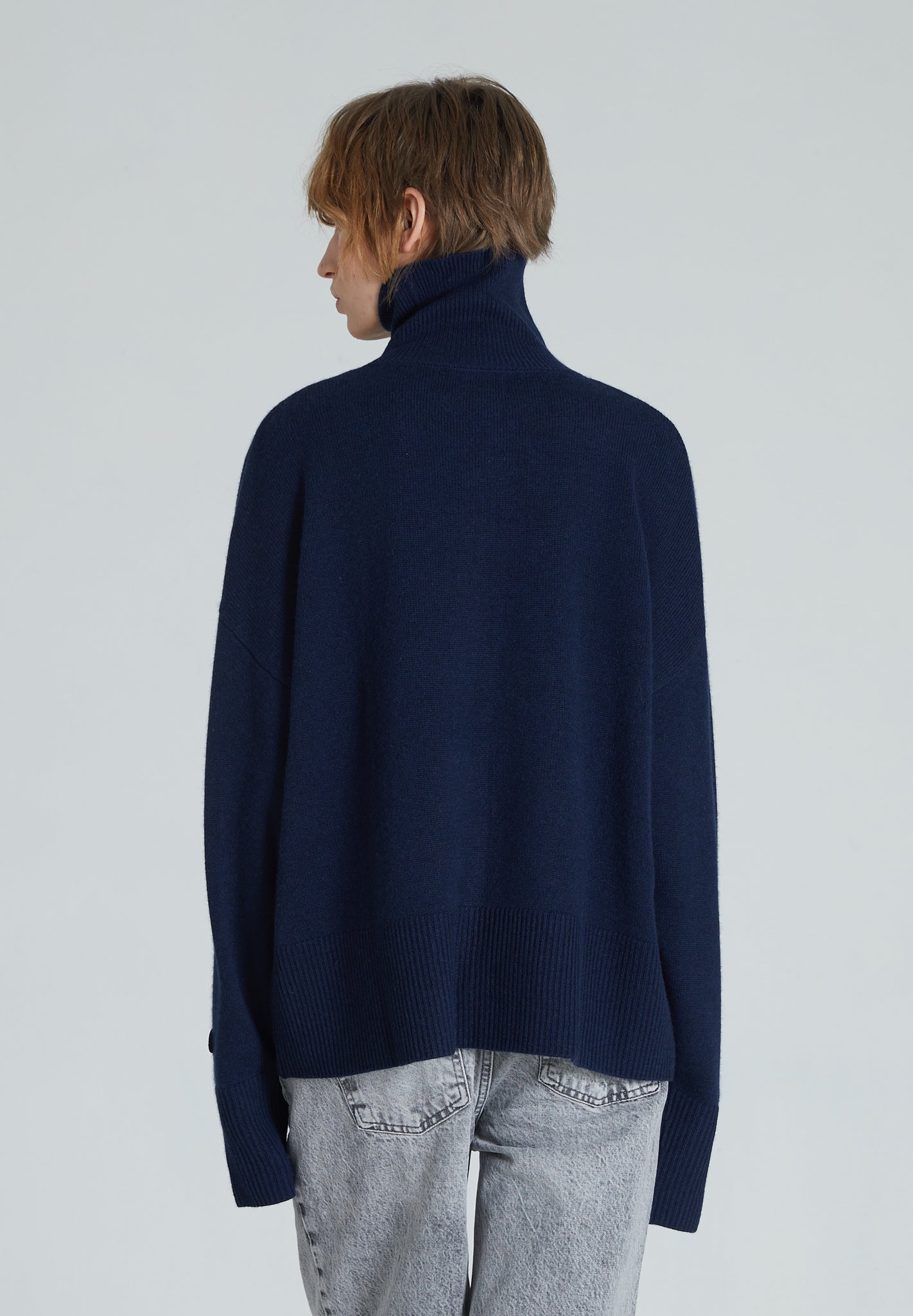 Back of navy turtleneck cashmere sweater with ribbed trims, displayed on a woman with grey jeans.